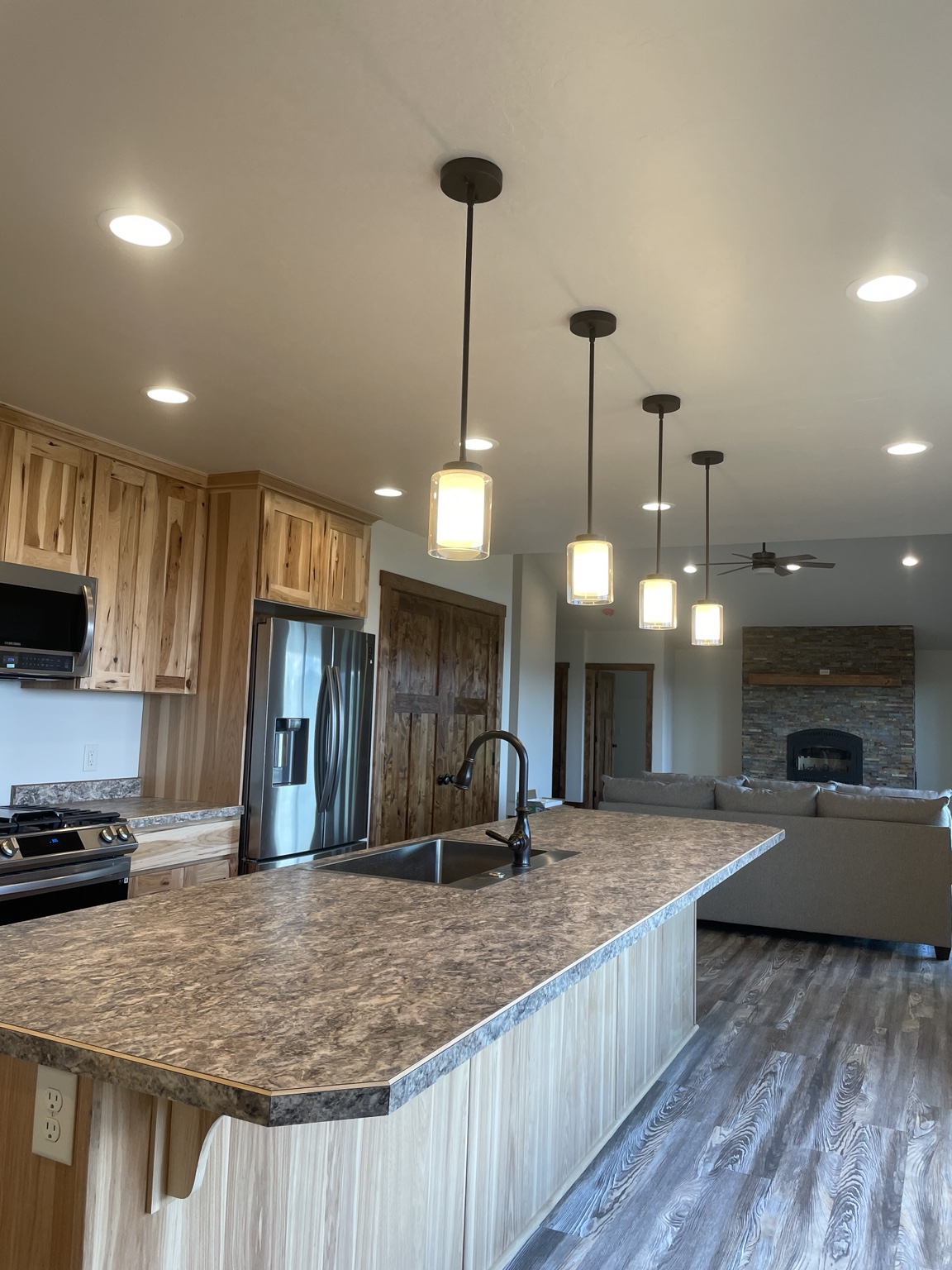Four illuminated glass pendants above a kitchen island, with recessed ceiling lights and wood cabinets
