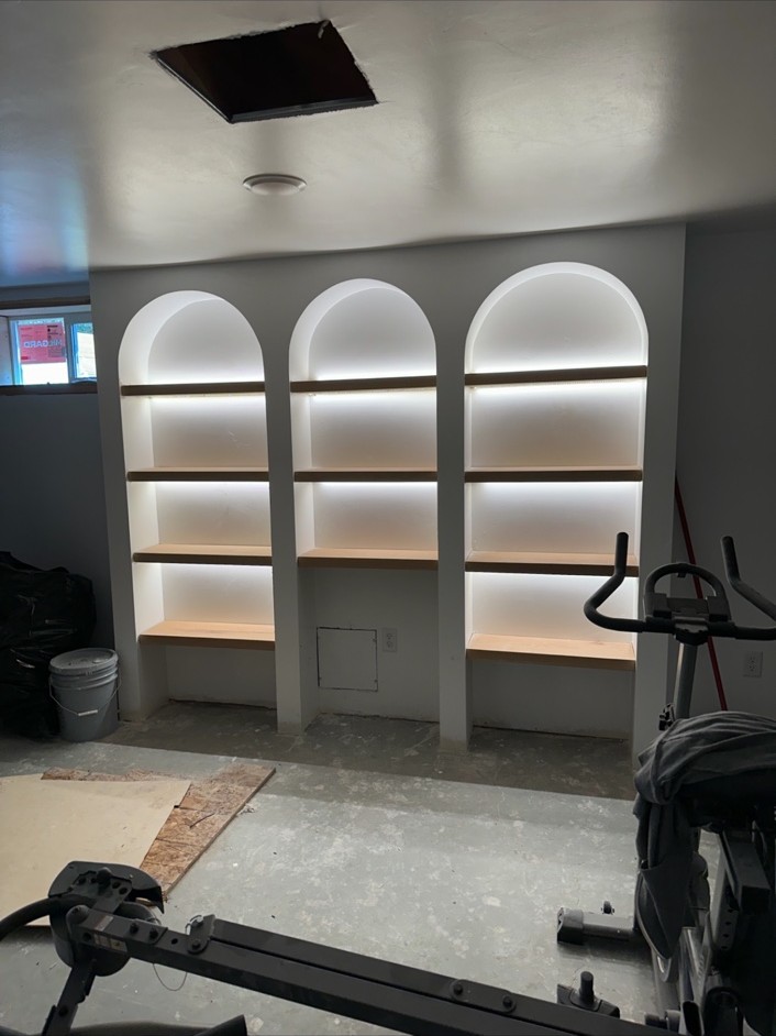 Three arched built-in shelving niches lit with warm strip lighting